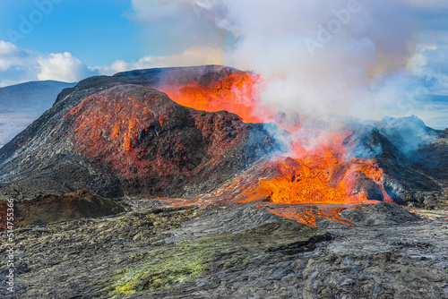 Volcanic eruption on the Reykjanes Peninsula in Iceland. Lava flows from volcanic crater. reddish liquid magma at the rim of the crater. cooled magma in front of the crater in reddish, greyish, green 
