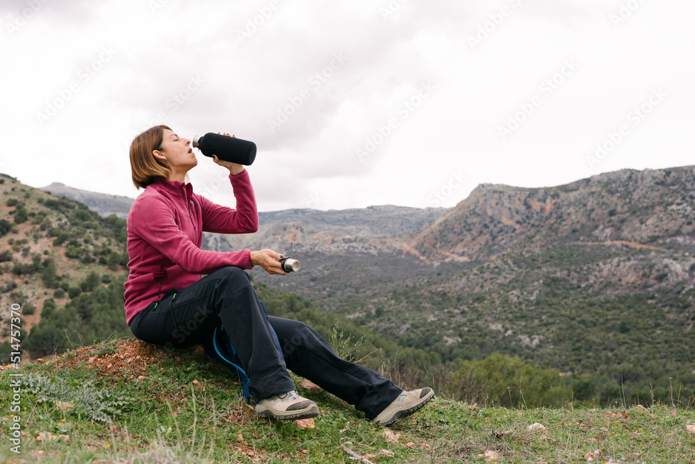 Woman sitting in the field drinking water from a steel bottle.