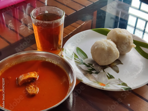 A glass of black tea (Sulaimani) with Delicious Kerala style breakfast dishes  white snacks(Kozhukatta) and fish curry served on a table photo