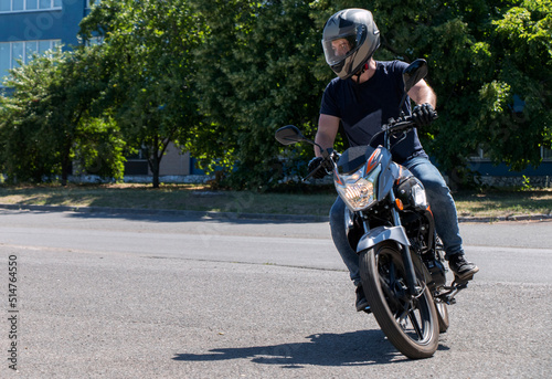 A guy in a helmet trains to ride a motorcycle, turns around on an empty asphalt road © OLEKSANDR