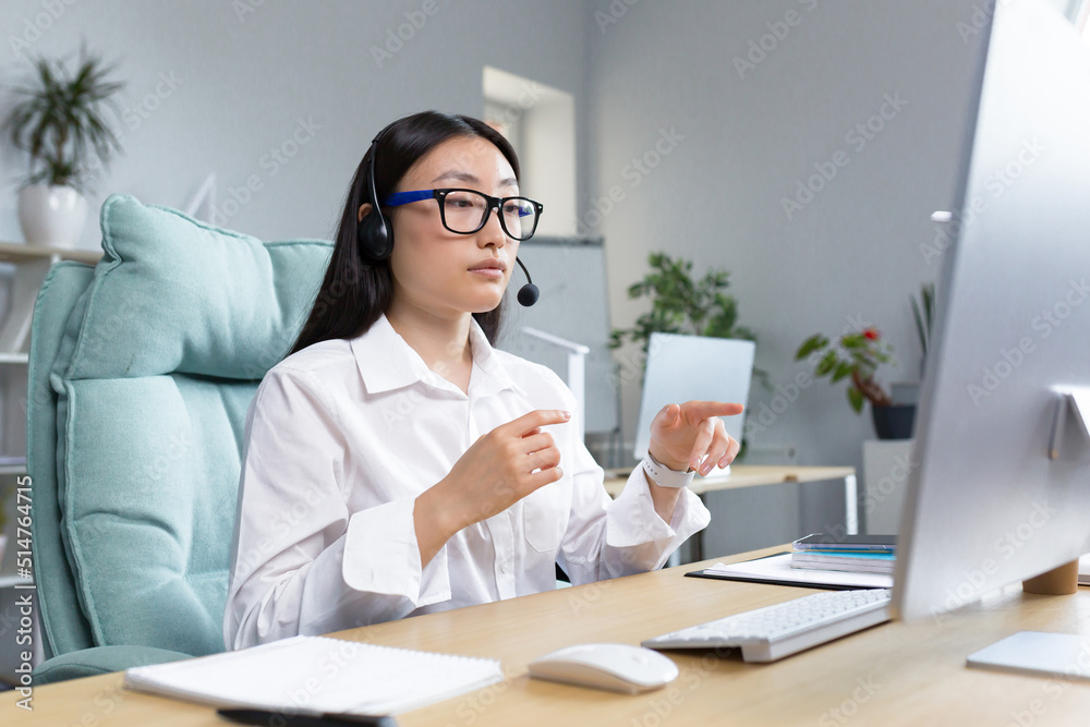 Consultant woman working remotely using headset for video call, talking to customers, helpline, Asian woman working in office. Consultant woman working remotely using headset for video call, talking to customers, helpline, Asian woman working in office.