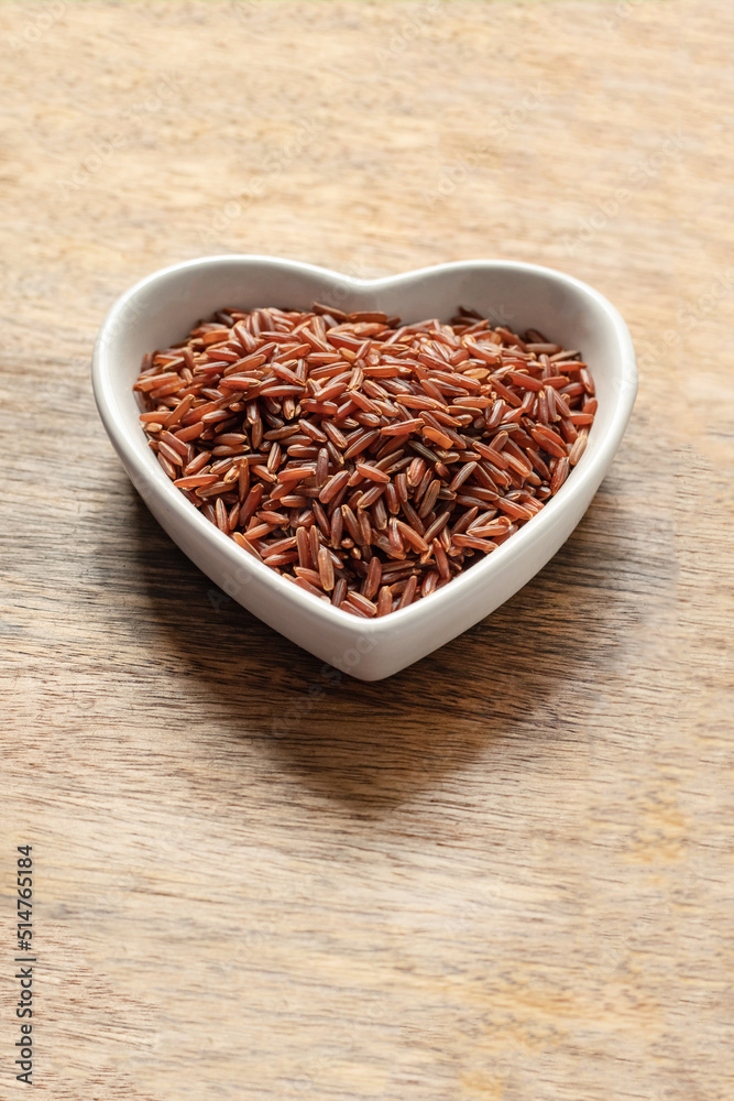 red long grains rice in heart shaped plate on wooden background close up red long grains rice in heart shaped plate on wooden background close up