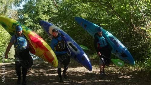 Wallpaper Mural Three recreational kayakers with helmets and life vests are moving from the river through the green wood, carrying kayaks and paddles, wide shot. Torontodigital.ca