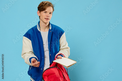 Fotografia a pensive student in a blue stylish bomber jacket stands with a notebook in his hands and looks away