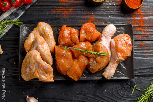 raw marinated chicken for barbecue, chicken fillet, chicken wings, chicken legs on dark plate on black wooden table top view