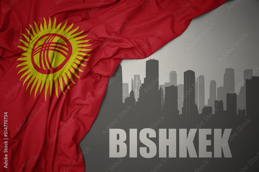 abstract silhouette of the city with text bishkek near waving national flag of kyrgyzstan on a gray background.3D illustration
