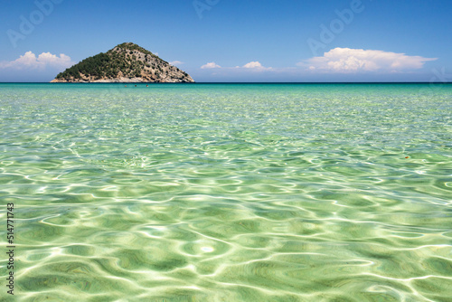 Shallow sea water surface with light reflection, little island in the background photo