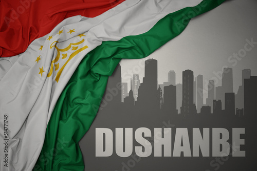 abstract silhouette of the city with text dushanbe near waving national flag of tajikistan on a gray background.3D illustration photo
