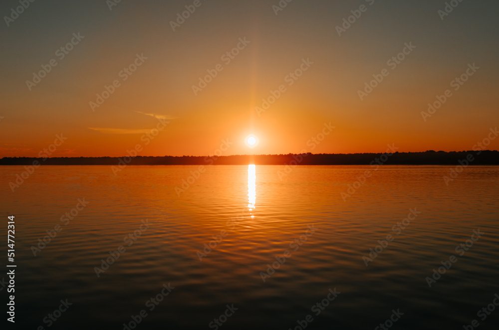 Beautiful colorful orange sunset on lake. Bright sun and reflection on water, natural landscape
