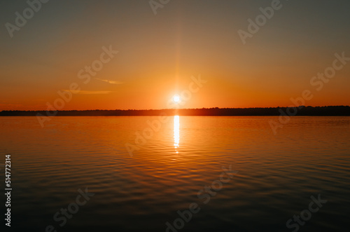 Beautiful colorful orange sunset on lake. Bright sun and reflection on water  natural landscape