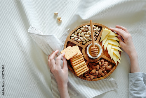 Wooden round menagerie in women's hands. Kitchen plate for snacks, table setting, natural style. Menazhnitsa with snacks, biscuits, cheese, nuts. High quality photo photo