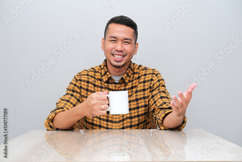 Adult Asian man sitting while holding a cup of drink and showing happy expression photo