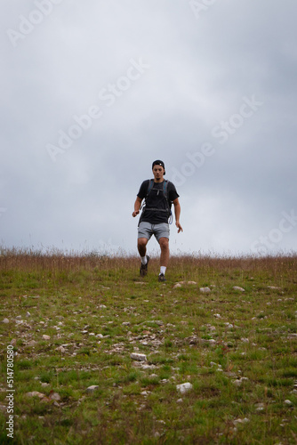 Swarthier type of man is running down a gravel hill, checking his every step to avoid injury. Active athlete runs over challenging terrain to improve fitness, coordination and precision of movement © Fauren