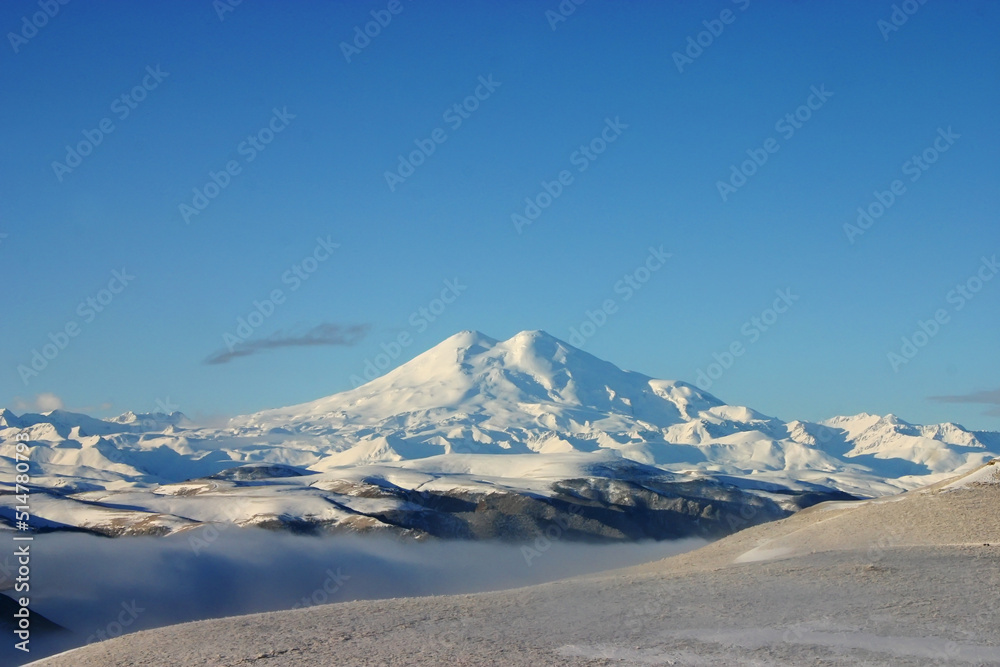 Elbrus is a high mountain. Dormant volcano. Mountain covered with snow, blue sky. Caucasus mountains. Fog and slopes