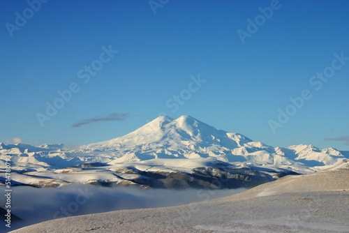 Elbrus is a high mountain. Dormant volcano. Mountain covered with snow, blue sky. Caucasus mountains. Fog and slopes © Vlad Kazhan