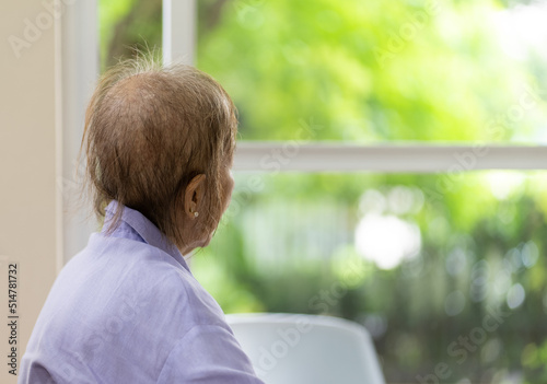 Senior Woman With Hair Loss After Chemotherapy From Breast Cancer Sitting Alone at Home looking Out of Window photo