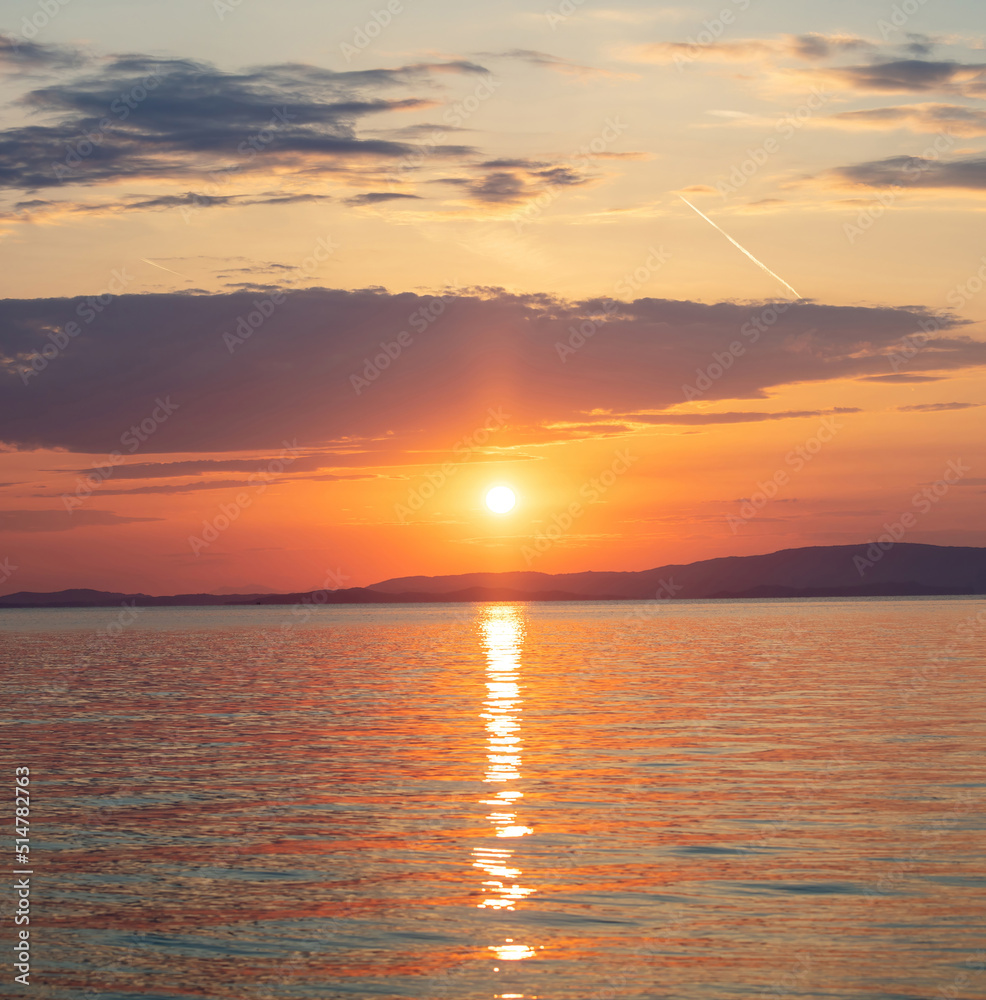 Sunset over Aegean Sea. Greece. Golden reflection on rippled ocean water. Dark land and colorful sky