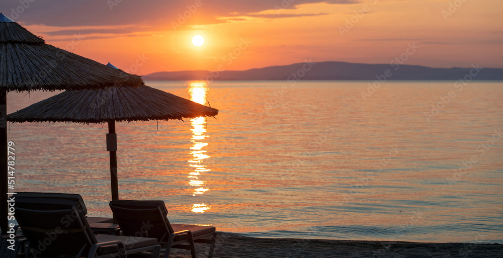 Sunset on the beach. Greece. Straw umbrella silhouette, golden reflection on rippled ocean water.