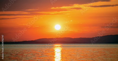 Sunset over Aegean Sea. Greece. Golden reflection on rippled ocean water. Dark land and colorful sky