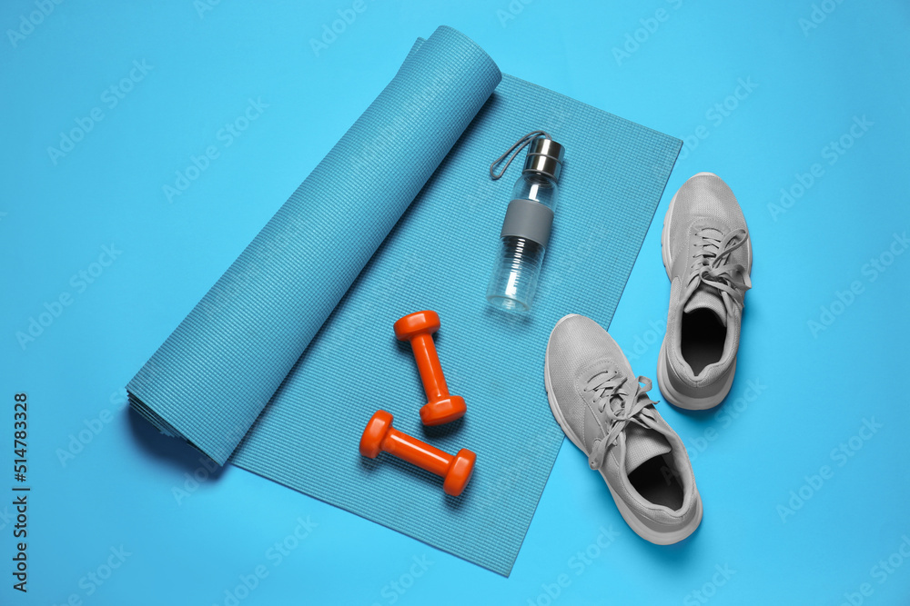 Naklejka premium Exercise mat, dumbbells, shoes and bottle of water on turquoise background, flat lay