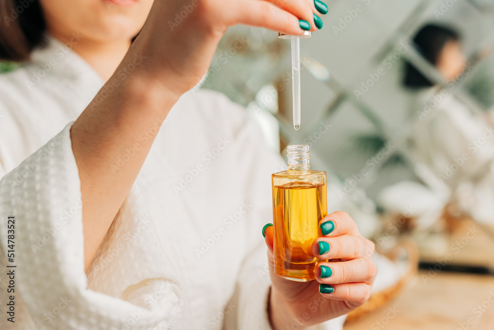 Fototapeta premium Facial Skincare. Happy Korean asian woman applying Facial serum using dropper standing in modern bathroom.