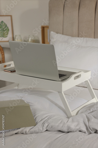 White tray with modern laptop and smartphone on bed indoors
