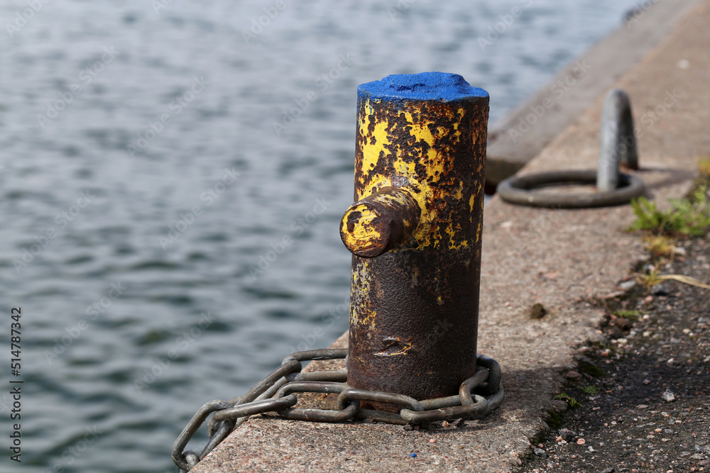 Small harbor architecture details in Helsinki, Finland, June 2019. Old rusty metal pole to which you can chain a boat. Also some concrete floor and calm sea are in the photo. Color image. Small harbor architecture details in Helsinki, Finland, June 2019. Old rusty metal pole to which you can chain a boat. Also some concrete floor and calm sea are in the photo. Color image.