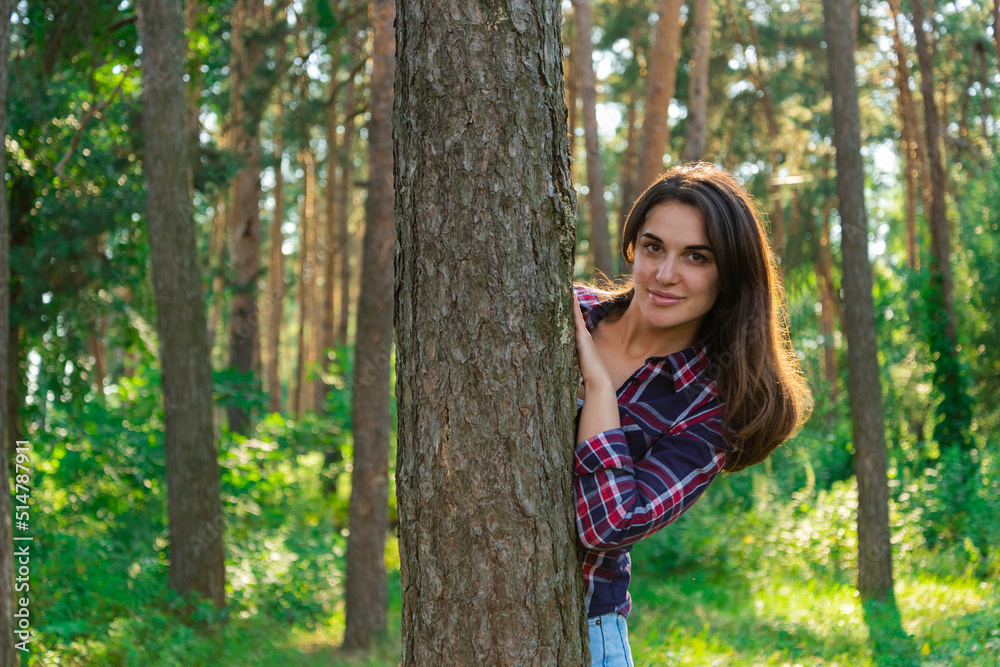 portrait of a young attractive brunette girl in the forest. girl peeking out from behind a tree portrait of a young attractive brunette girl in the forest. girl peeking out from behind a tree