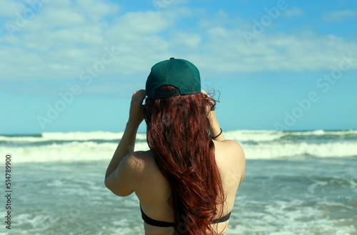red-haired girl in a cap looks into the sea