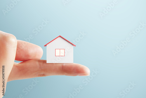 Close up of finger holding tiny house on blue background with mock up place for advert. Loan and insurance concept.