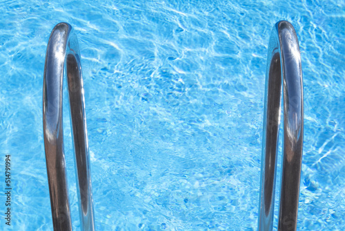 Close up top view descent to bright blue pool full of sparkling water. Infvitation to chill and have cooling party on holiday,water rest on hot day. Copy space. Pool stair railing. Cleaning service. photo