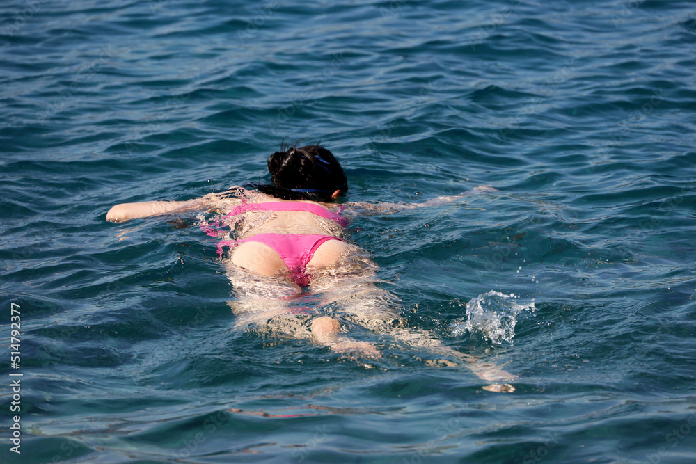 Snorkeling and diving in a sea, girl in pink bikini swimming in mask in blue water. Beach vacation in summer