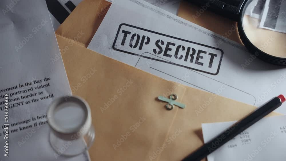 Slow pan across different top secret classified documents laid on office desk. Papers inside manila envelopes and folder with sensitive information. Leaked or uncovered memos by military or government