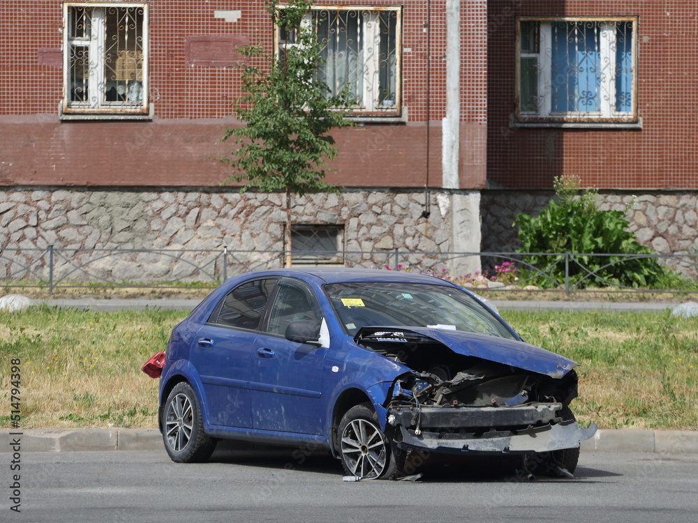A broken abandoned blue car is parked under the windows of a residential building, Rossiyskiy Prospekt, St. Petersburg, Russia, July 2022