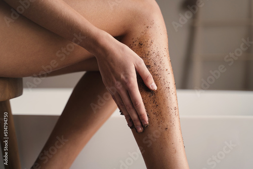 Close-up of woman hand scrubbing legs in bathroom during anti-cellulite massage with coffee scrub