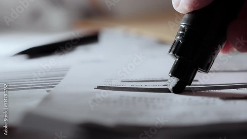 Extreme close up as black marker draws black line on redacted censored text memo. Hand using pen to erase or censor information from top secret or classified paper. Leaked or declassified document