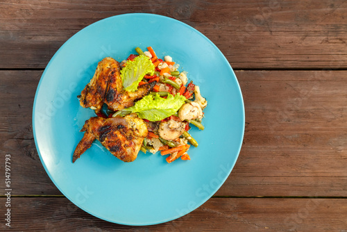 Blue plate with chicken and vegetables on a wooden table. Horizontal photo