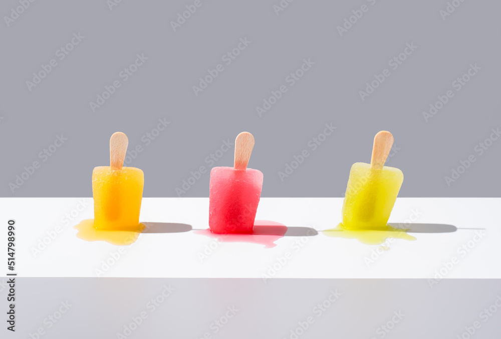 Paletas de hielo de colores derritiéndose. Palitos de helado naranja, rojo y amarillo sobre fondo gris. Concepto de verano Paletas de hielo de colores derritiéndose. Palitos de helado naranja, rojo y amarillo sobre fondo gris. Concepto de verano