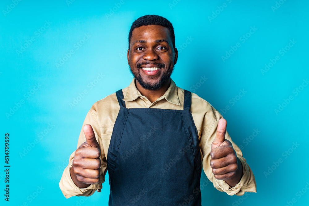 african american man in black apron is ready to spring season in blue studio background showing thumbs up gesture with hands african american man in black apron is ready to spring season in blue studio background showing thumbs up gesture with hands