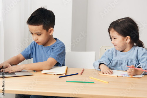 children draw with colored pencils sitting at the table and talking to each other