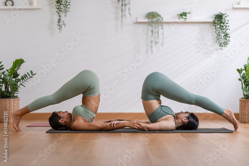 Couple and paired Asian young woman on yoga mat doing breathing exercise yoga Halasana or Plough pose together.Yoga meditation of two healthy female balancing body and relax cozy home. Wellness life photo