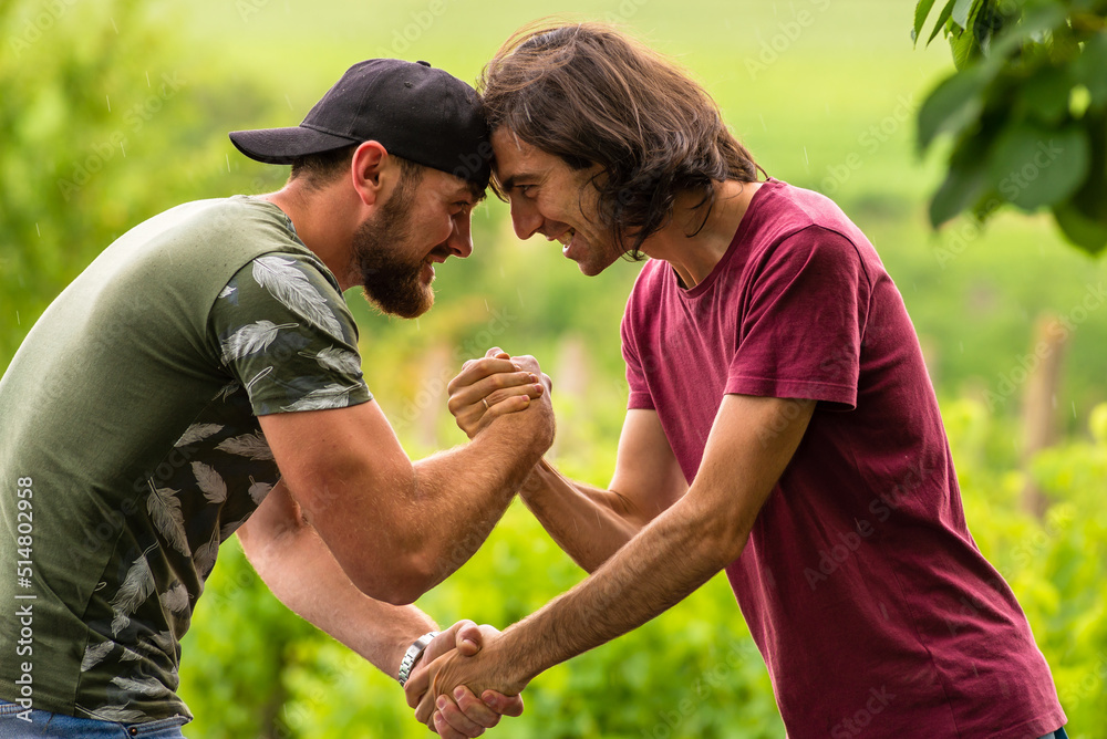 two male brothers shake hands smiling in natural background, dressed in