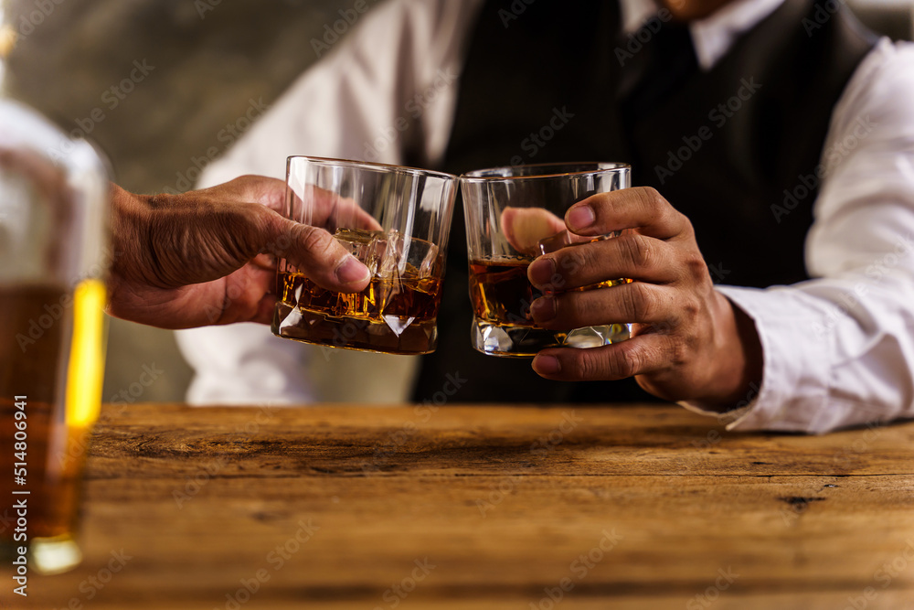 Two hands clink glasses of whiskey wiskey on the couch, cozy. Bar drinking menu. Two hands clink glasses of whiskey wiskey on the couch, cozy. Bar drinking menu.
