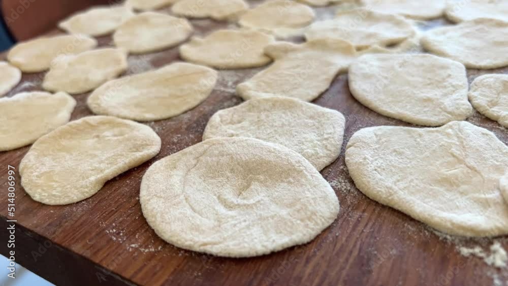 grandmother prepares delicious dumplings or pies or dumplings for her grandson she shakes dough, cuts it into pieces and sculpts on the table there are circles of dough she is sprinkled with flour