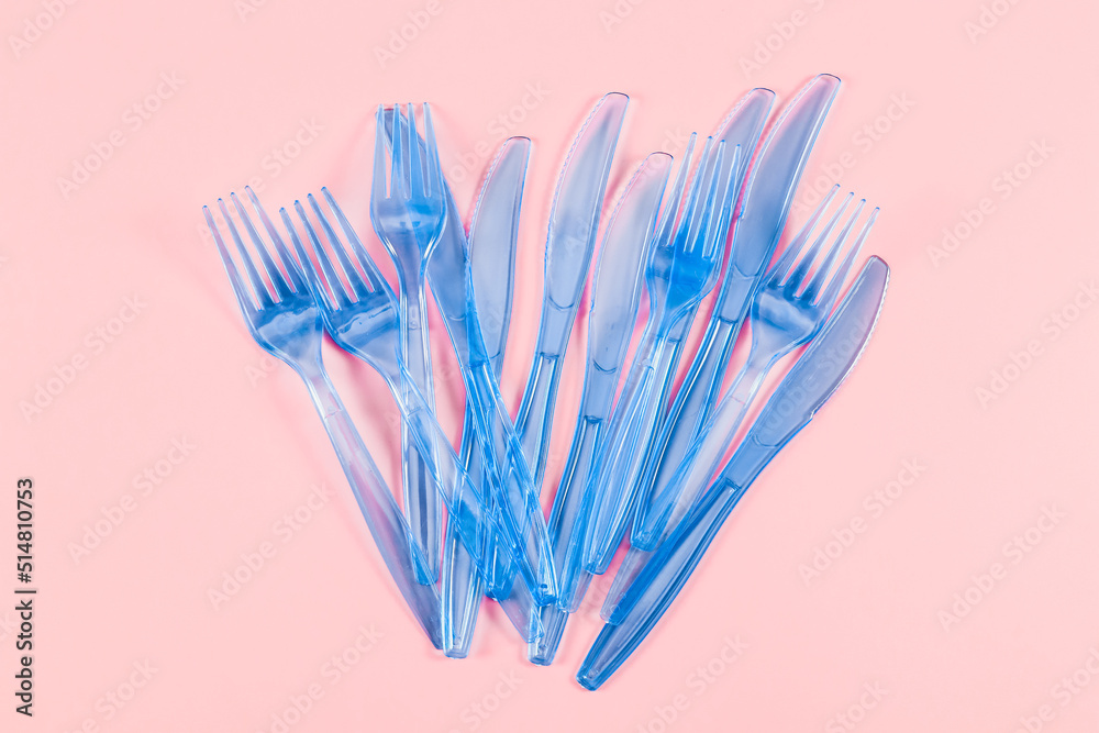 A set of plastic transparent knives and forks lie in the center on a pink background A set of plastic transparent knives and forks lie in the center on a pink background