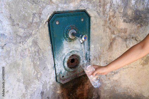 Woman hand fills a plastic bottle of water from a fountain in the wall. Thirsty and water crisis concept. photo