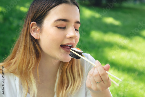 A young woman eating sushi in nature, maki roll close-up.