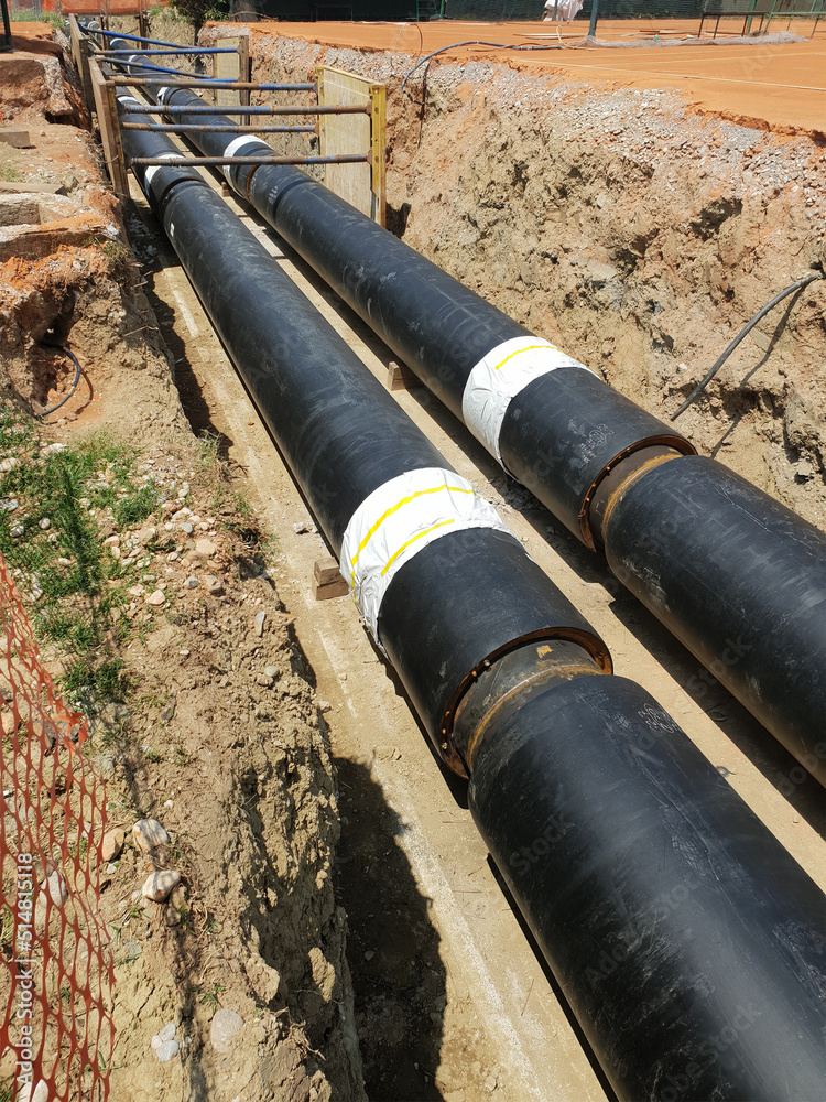 Laying heating pipes in a trench at construction site. Laying heating pipes in a trench at construction site.