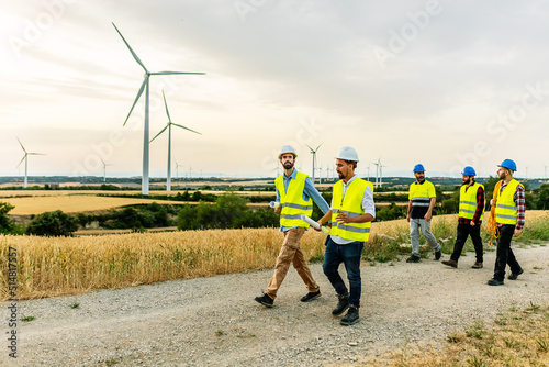Group of technicians and engineers people walking on a field path at a wind farm - Renewable and alternative energy concept