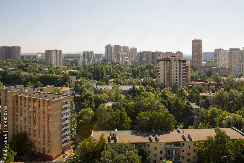 The urban landscape is the city of Reutov with residential buildings among the lush green foliage of trees and a clear blue sky on a summer day and a space for copying